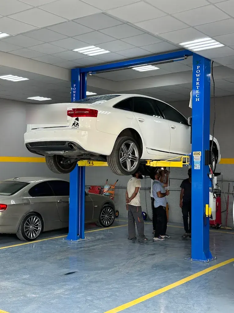 White Audi A6 raised on the lift for undercarriage service at Madeena Al Amwaj Auto Workshop